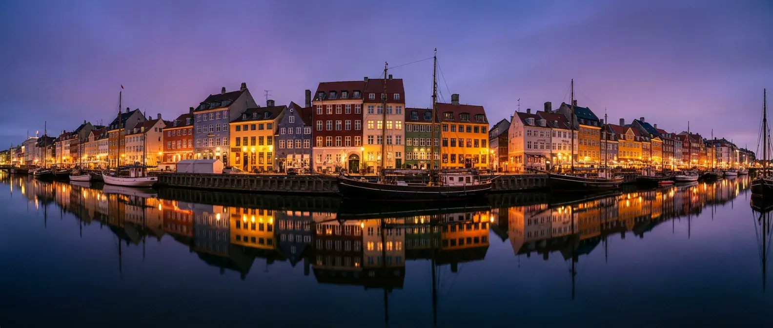 Nyhavn i København i skumringen. Oplyste karréhuse og fortøjede træskibe spejler sig i kanalen.